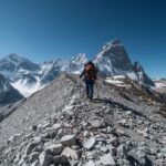 High altitude hiking on steep mountain trail with climber using trekking poles and snow peaks in distance